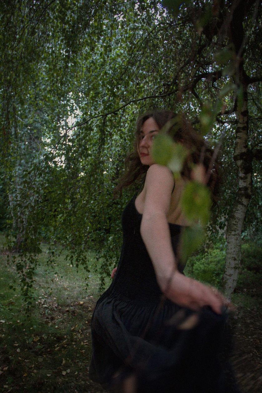 Woman in a black dress among birch leaves